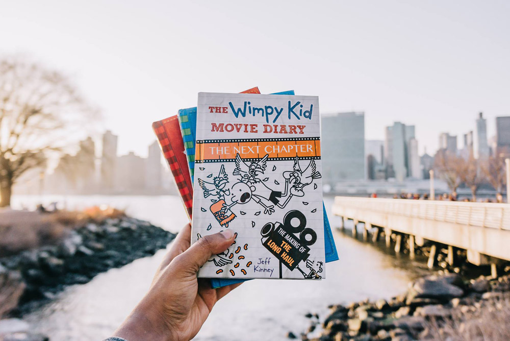 Image of person holding Wimpy Kid books with city skyline in the background