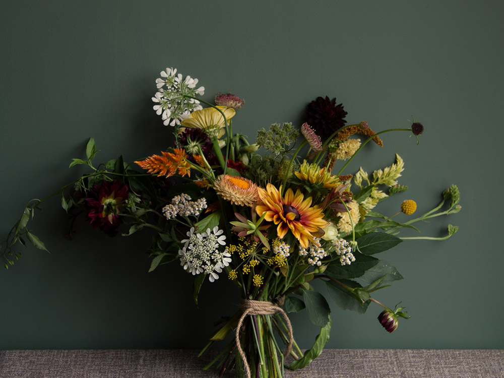 Image of a moody bouquet next to a deep green wall