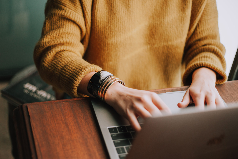 Image of person typing on laptop in a mustard sweater