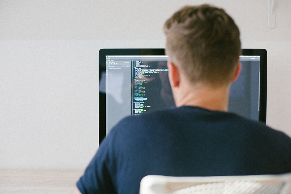 Image of a man looking at a computer with the code on it